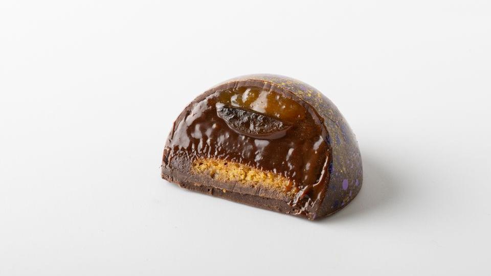 A singular chocolate cut in half showing the various layers of it's content.