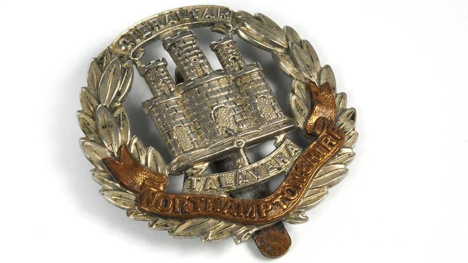 A badge feature the insignia of the Northamptonshire Regiment, which includes a castle in the middle.