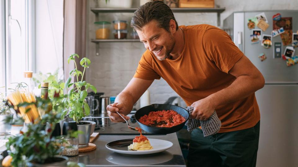 Smiling young man preparing and tasting spaghetti with tomato sauce