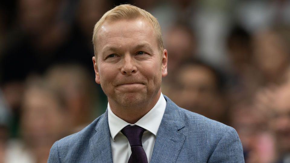 Sir Chris Hoy wears a light blue suit and maroon time and is facing the camera while photographed in the royal box at Wimbledon Centre Court in 2024