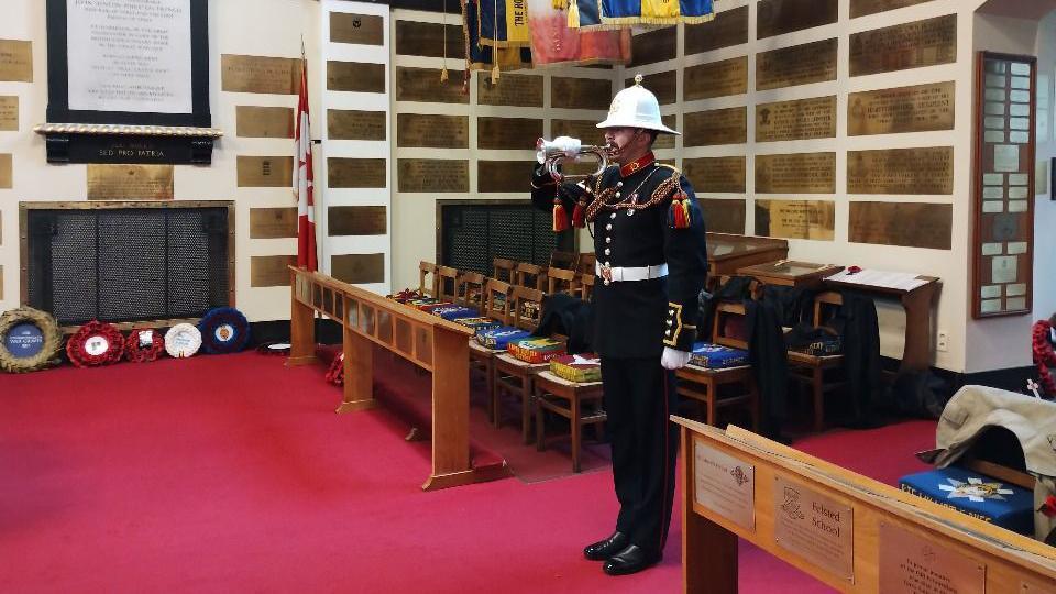 A soldier in ceremonial uniform plays a brass instrument.