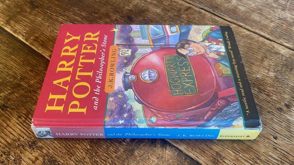 A first-edition copy of Harry Potter and the Philosopher's Stone on a wooden table.