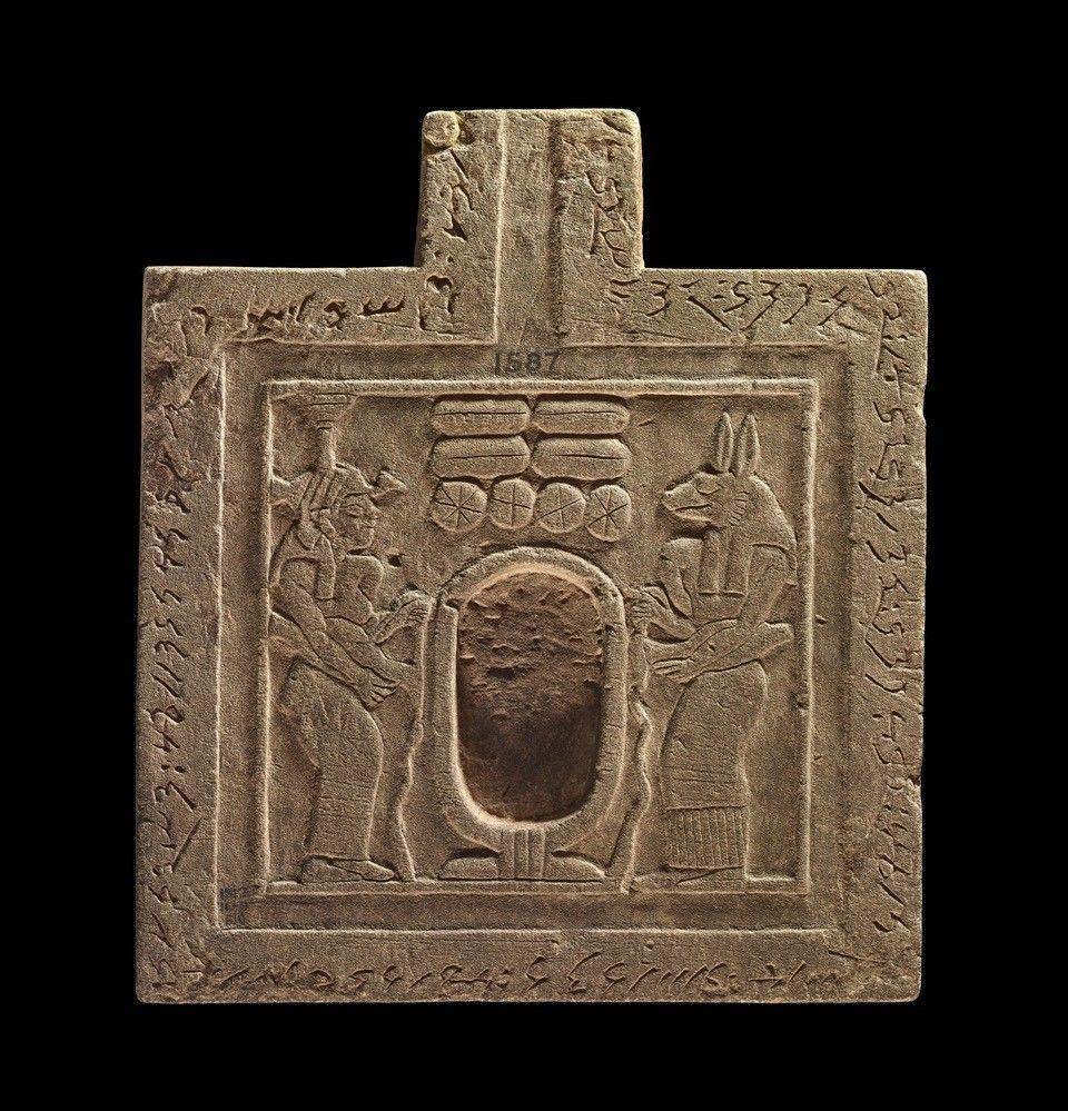 A sandstone table on a black background. The table features inscriptions and depictions of deities