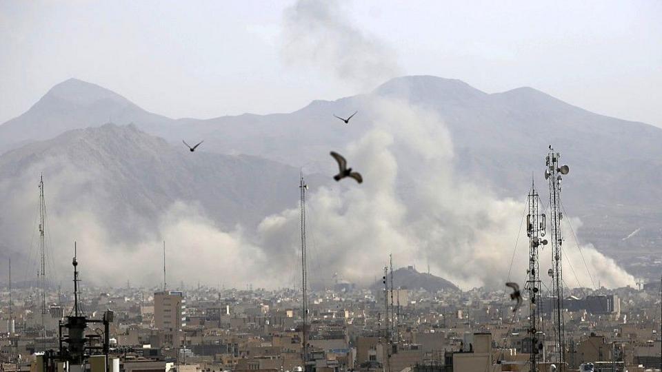 plumes of smoke rise over Tehran in Iran, with mountains seen silhouetted in the background.