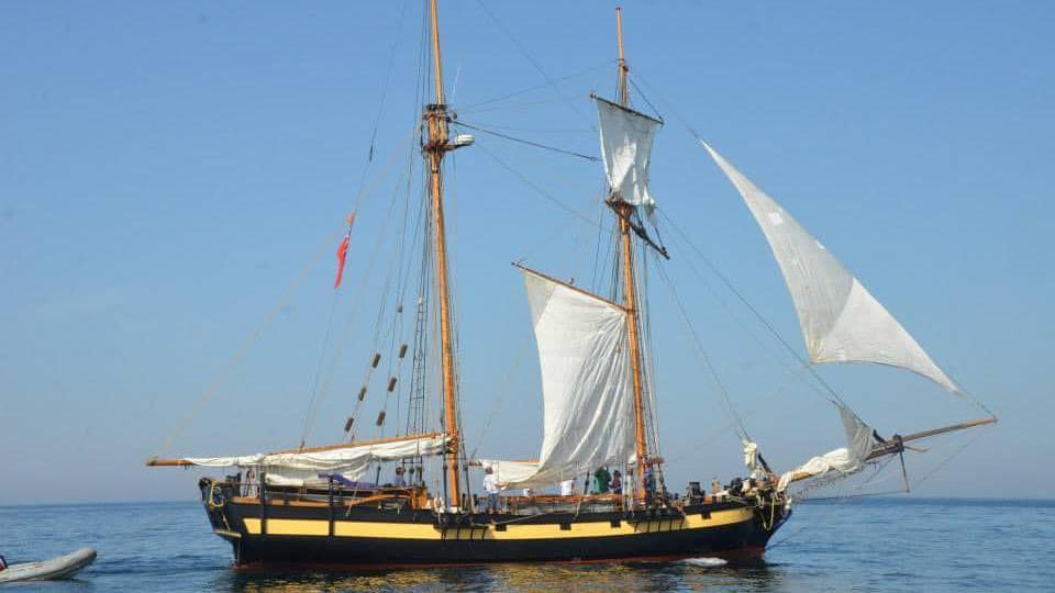 A small, tall ship, with white sails, filled with the wind, and rigging. 