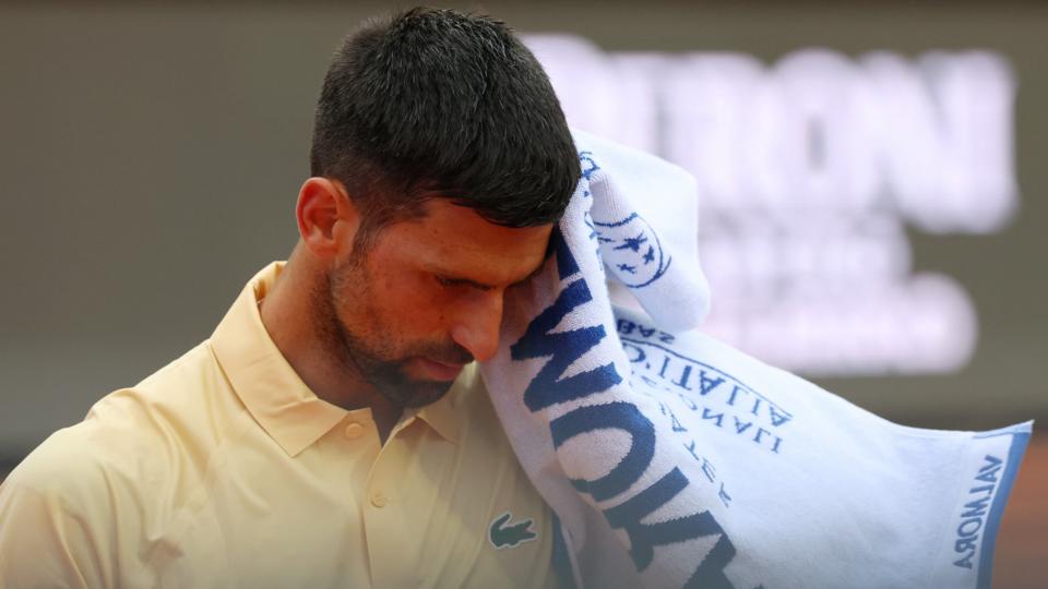 Novak Djokovic reacts during the Italian Open, raising a towel to his face while wearing a yellow tennis shirt