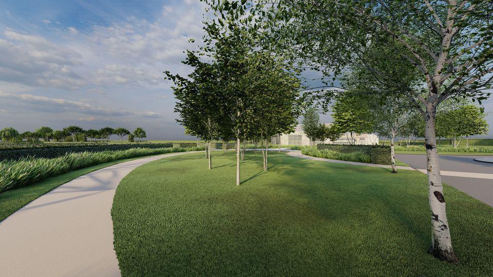 A park with green grass and trees and a concrete walkway with green paths along it and a building in the background 