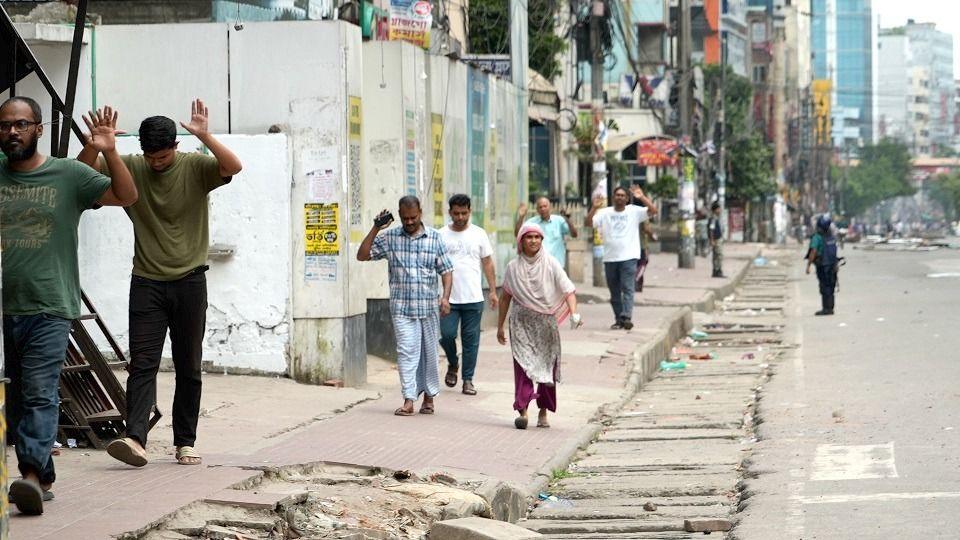 people in Dhaka walk past a soldier with their hands up