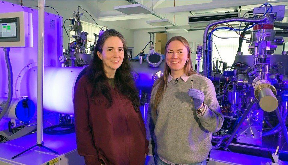 Prof Kelly Morrison (left) with Dr Naëmi Leo, in front of the Loughborough University nanolithography system. Dr Leo holds the chip that features the image of "the world’s smallest violin"