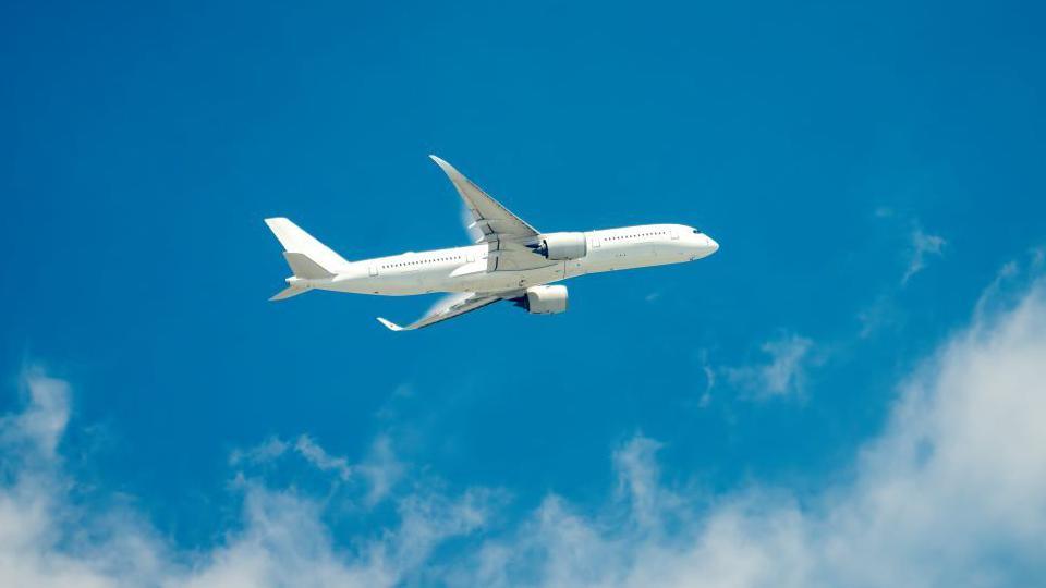 A white aeroplane is travelling through a blue sky with white fluffy clouds.