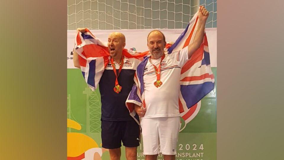 Andy Taylor and Alan Cowling with a Union Flag draped over their shoulders and wearing bronze medlas