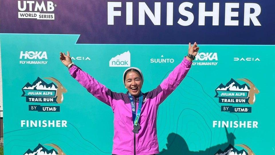 Fatima Painda wearing a pink jacket and a medal around her neck, posing with her hands in the air