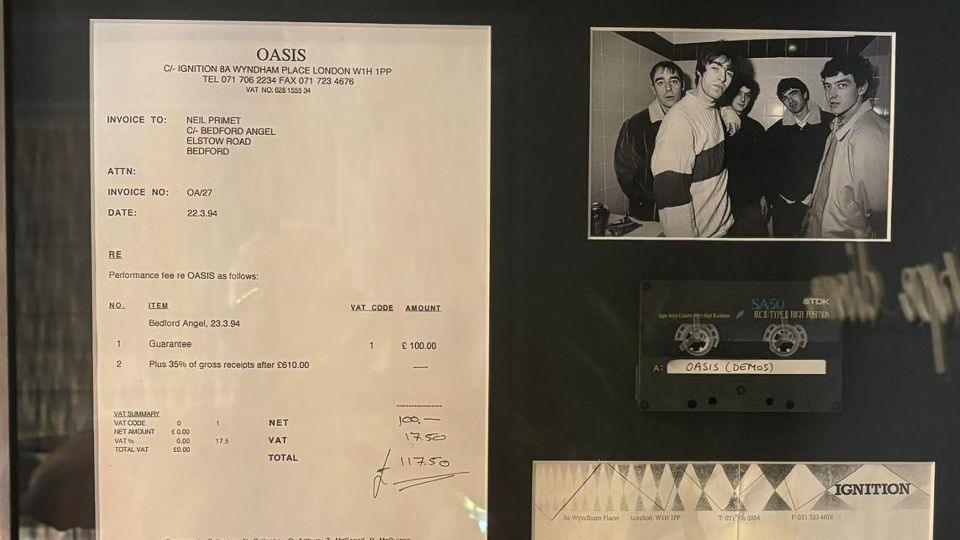 Framed memorabilia from Oasis's performance in Bedford, including the invoice and a demo cassette