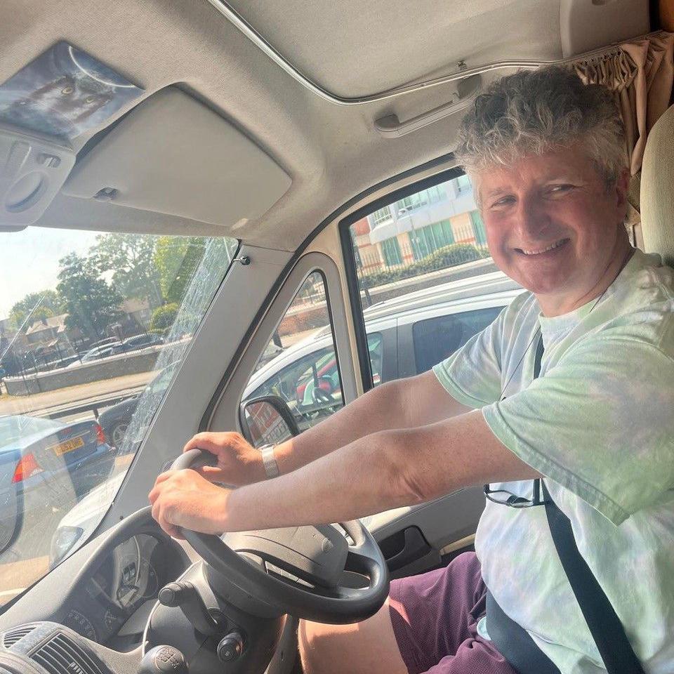 Alan Smith smiles as he sits in the driver's seat of his caravan.