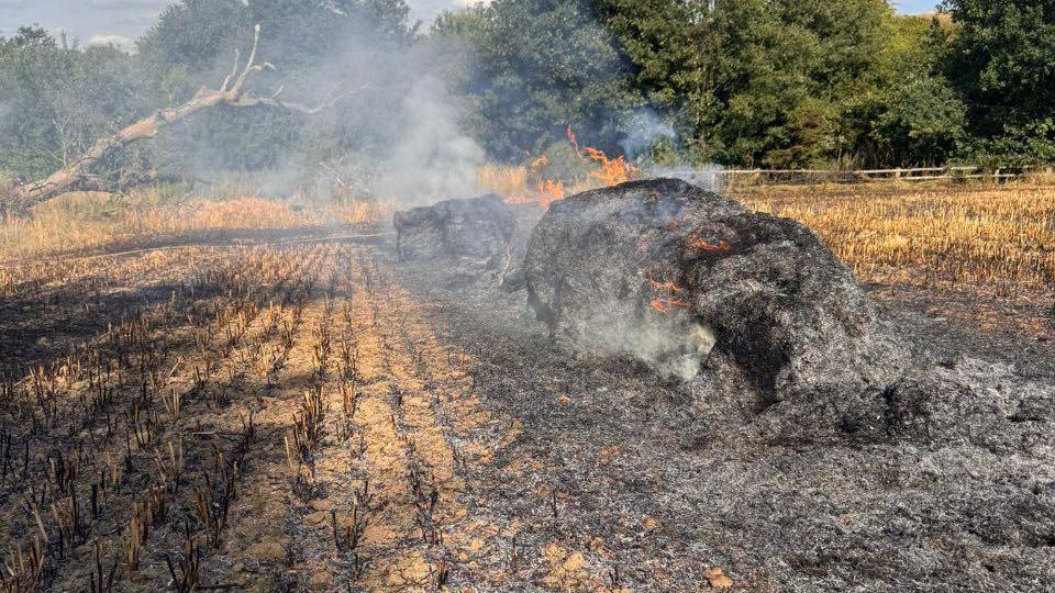 A scorched crop field with burning hay bales