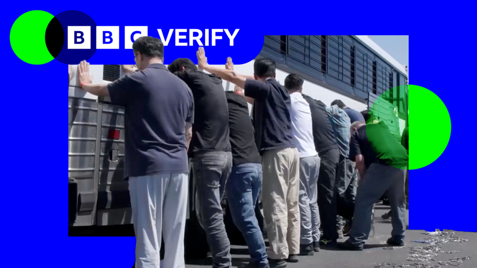 A still frame from a video shows a group of men, with their backs to the camera and hands on the side of a white coach with black bars on its windows during an immigration raid at the Hyundai-LG vehicle assembly plant in Ellabell, Georgia.
The men are in casual clothing, mostly jeans or slacks and T-shirts.