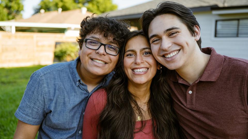 Multigeneration siblings looking at a camera in the front garden and smiling.