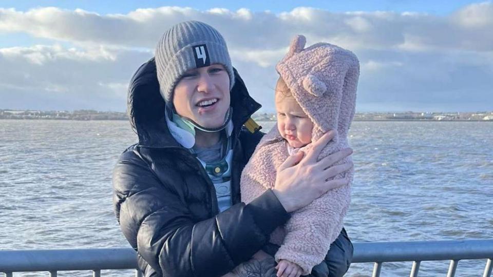 Liam McCracken, who is standing up and holding his daughter, is still wearing a neck brace as they pose for the photograph along the coast. 