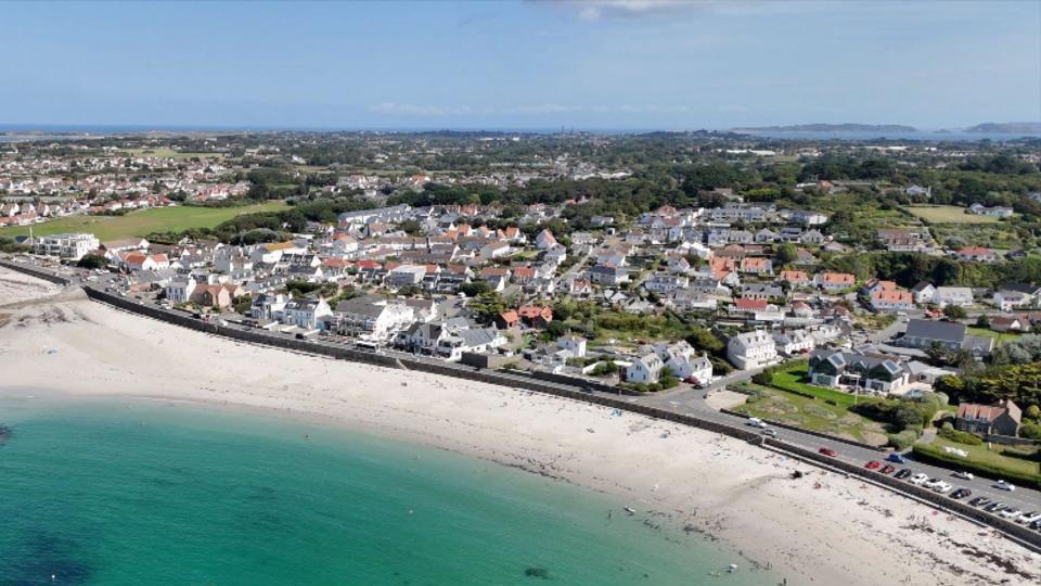 An aerial view of Guernsey with the sea on the left-hand corner and houses on the right hand corner.
