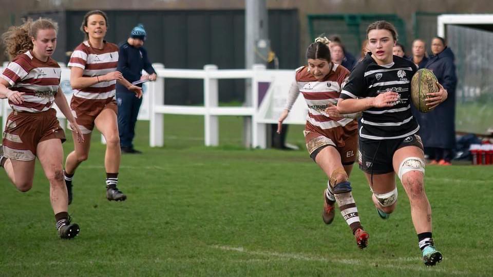 A woman in rugby kit races away from her opponents