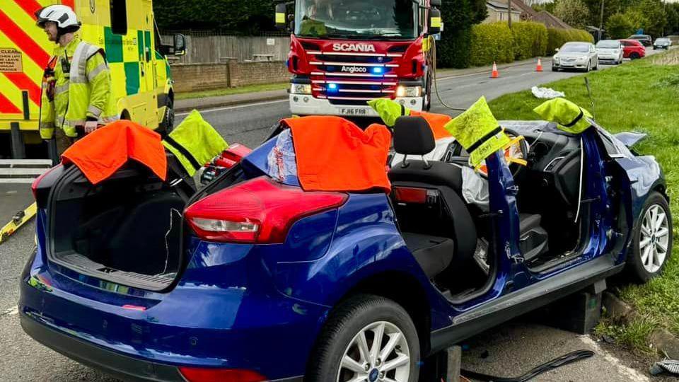 Firefighters by a car that has had its roof taken off 