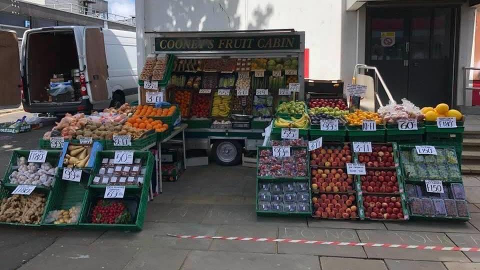 Several carts are stacked on top of each other, displaying colourful and neatly arranged fruit and vegetables. There is a cart that reads 'COONEY'S FRUIT CABIN'.