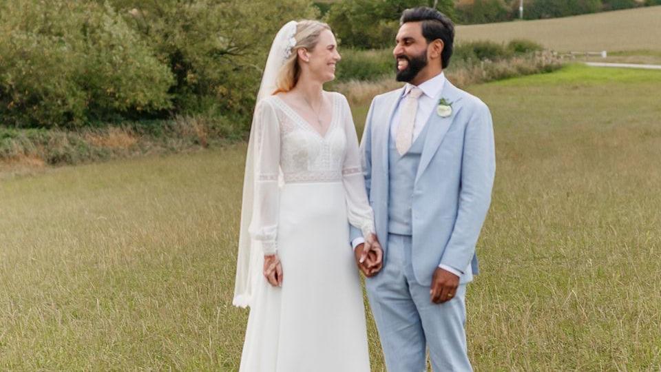 Newly married couple in wedding attire stood in field