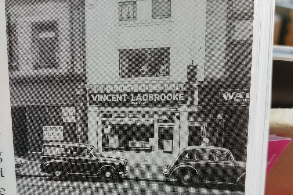 Two vintage cars parked in front of a shop with signage saying TV demonstrations daily, Vincent Ladbrooke