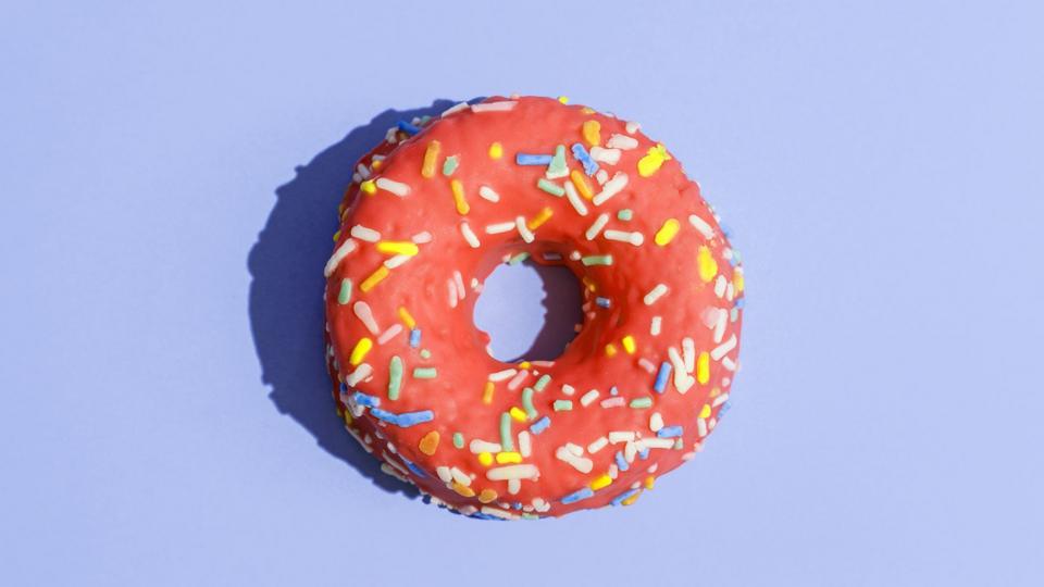An iced doughnut with sprinkles on a purple background.