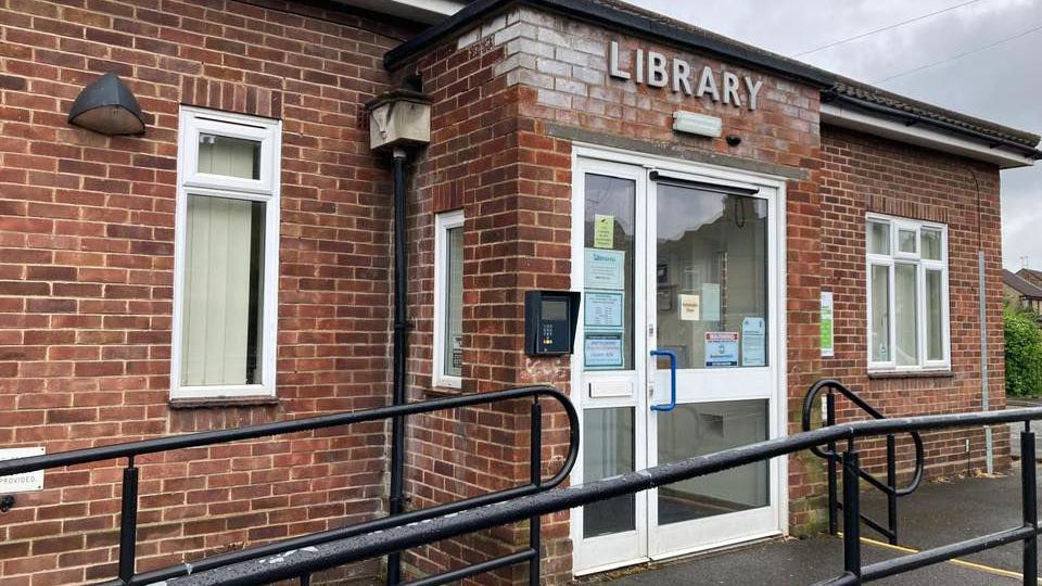 Outside of the library building, it is a small brick building with a capital letter sign saying LIBRARY. 