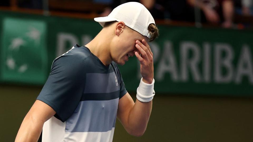 Holger Rune holds his hand over his eyes as he walks off the court with injury