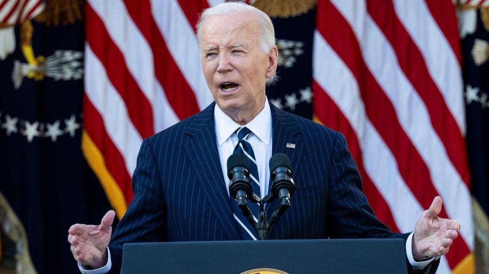 Joe Biden gestures as he stands at a lectern in front of American flags