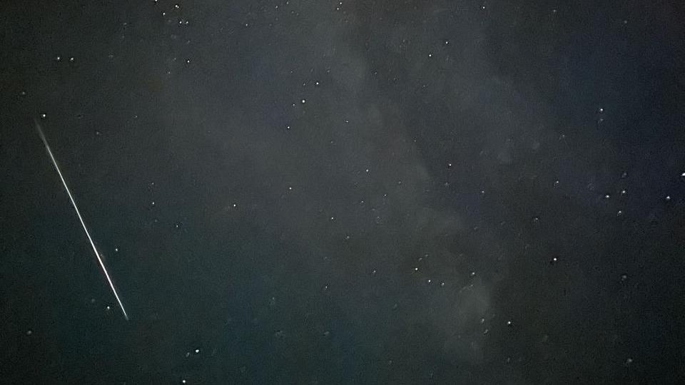 A night sky, a shooting star moves on the left side of the image