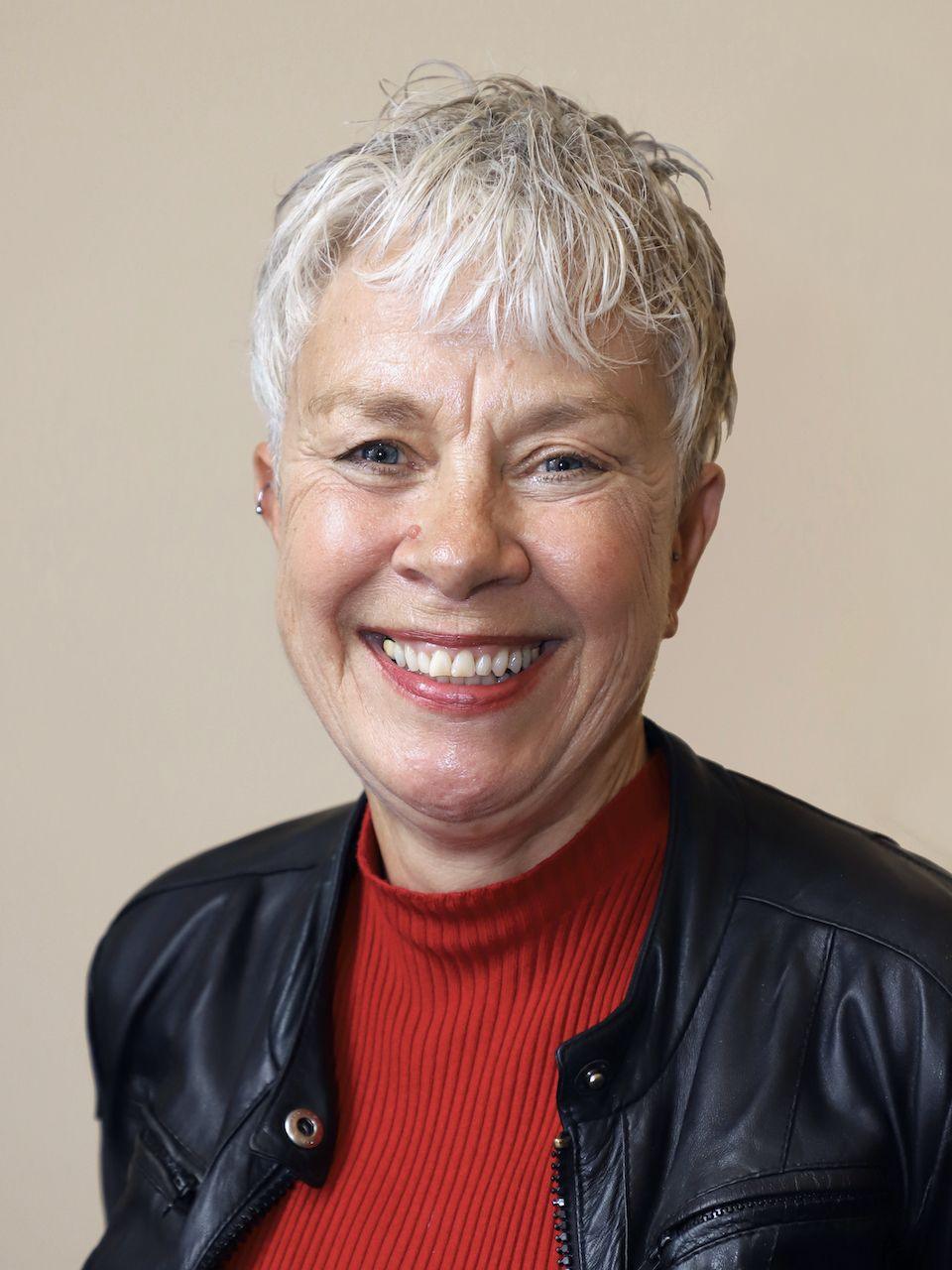 A grey-haired woman in a black jacket with a red jumper