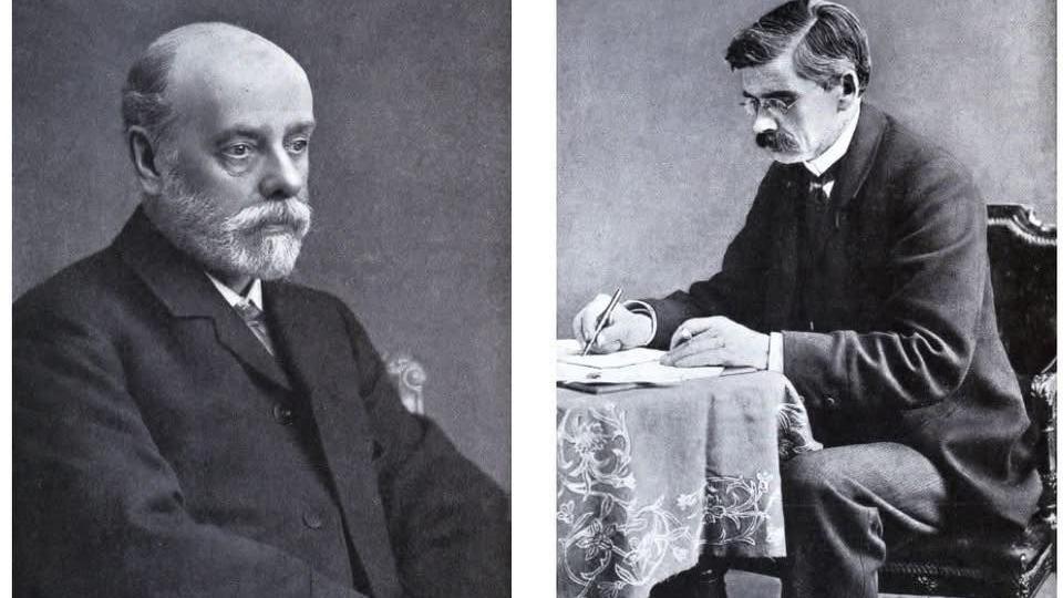 Vero Charles Driffield (left) is bald, has a white beard and is wearing a dark suit, with white shirt and patterned tie. Ferdinand Hurter has short dark hair with flecks of grey, round spectacles and a moustache. He wears a winged collar with a Victorian tie and is seated writing at a desk with a table cloth.