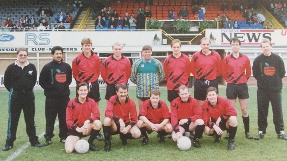 A group of men in red football outfits posing in two rows, the first row is kneeling while the back row is standing behind them.