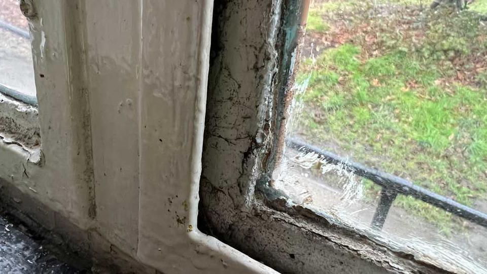 An old metal framed 1950s window with peeling white paint and water damage