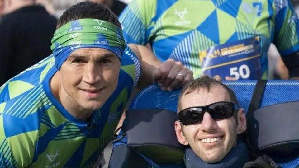 Kevin Sinfield (left) and Rob Burrow (R) wearing green and blue running gear, including a headband. Rob has sunglasses on and is sat in a chair.