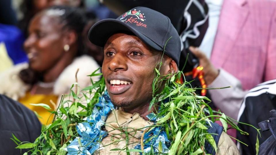 Kenyan World Marathon Record holder Sabastian Sawe smiles with wreaths laid around his neck.