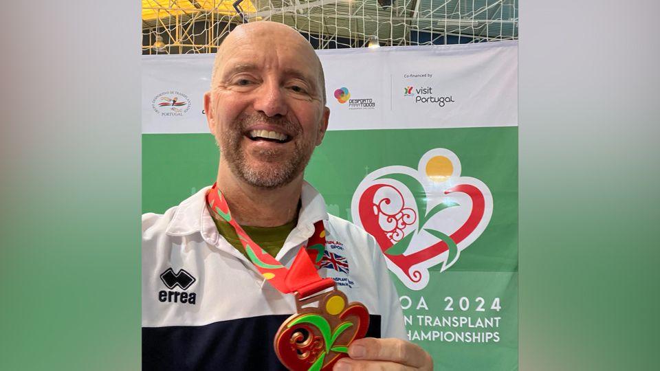 Andy Taylor holding his bronze medal and smiling