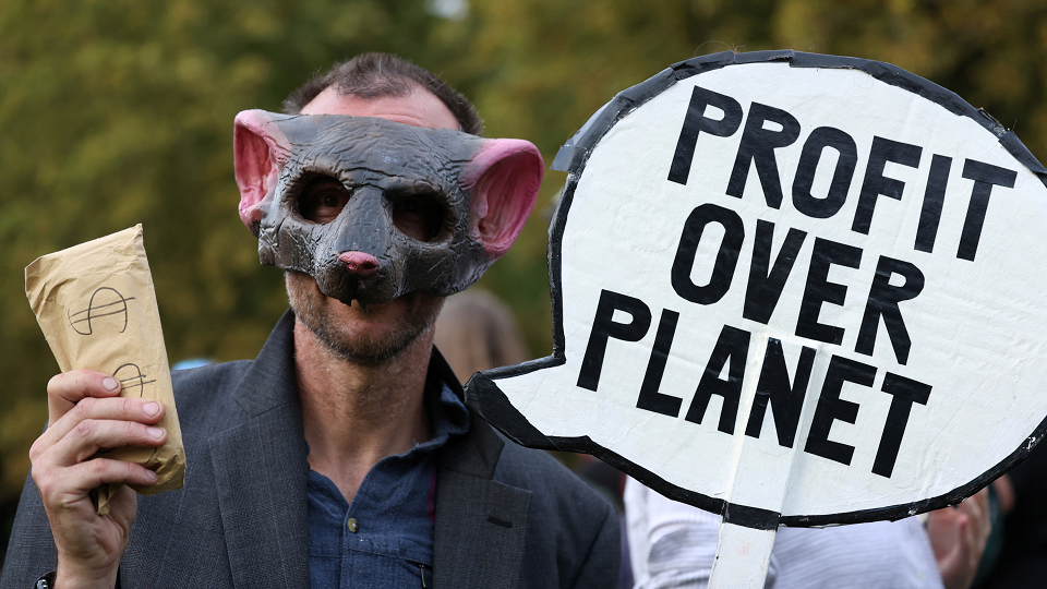 An Extinction Rebellion activist wears a pig mask and holds a sign which reads "profit over planet".