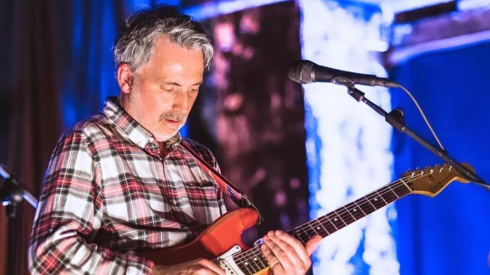 Guitarist Paul Casey playing on stage, wearing a checked shirt