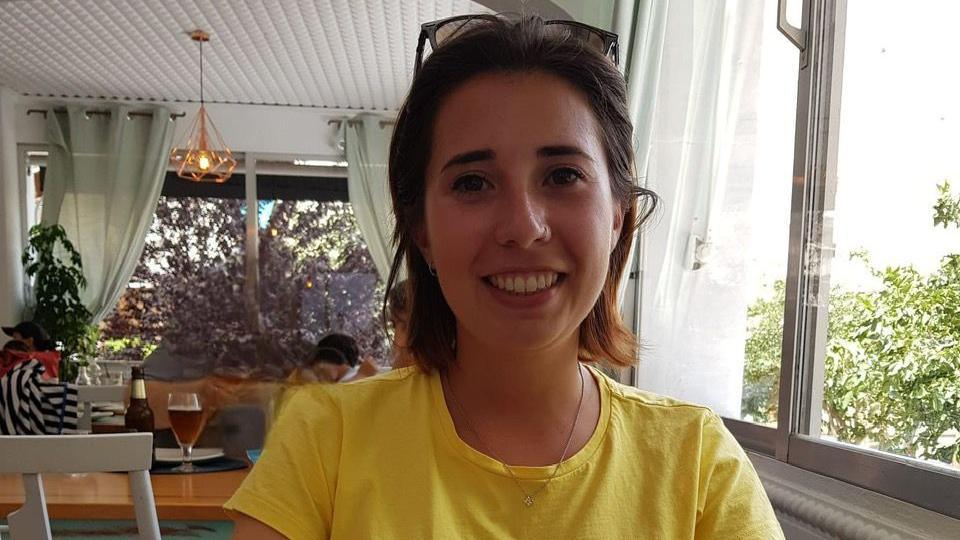 Marta Elena Vento smiles at the camera in a dining room. She has short, brown hair and wears a yellow T-shirt.