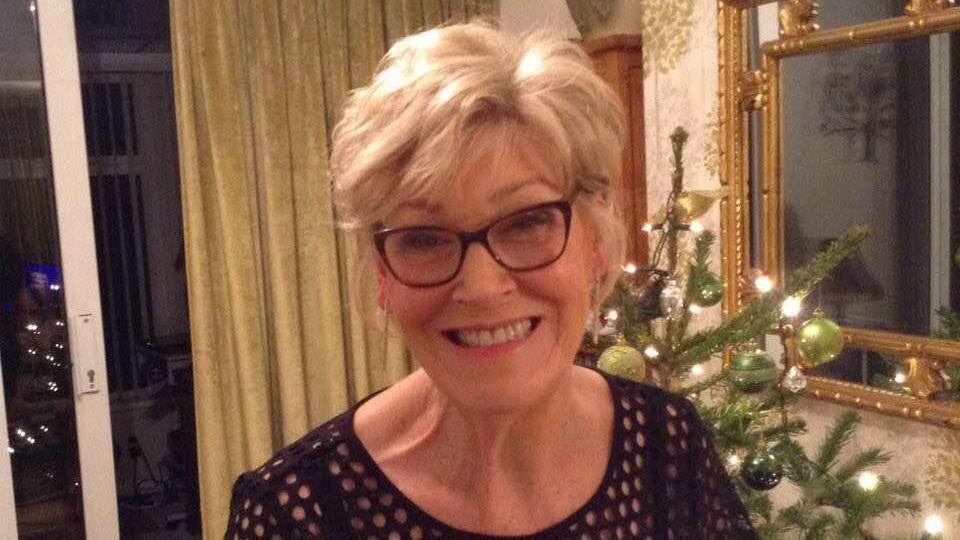 Rosemary McGerty standing in front of a Christmas tree and smiling at the camera. She has short blonde/white hair and is wearing dark glasses.