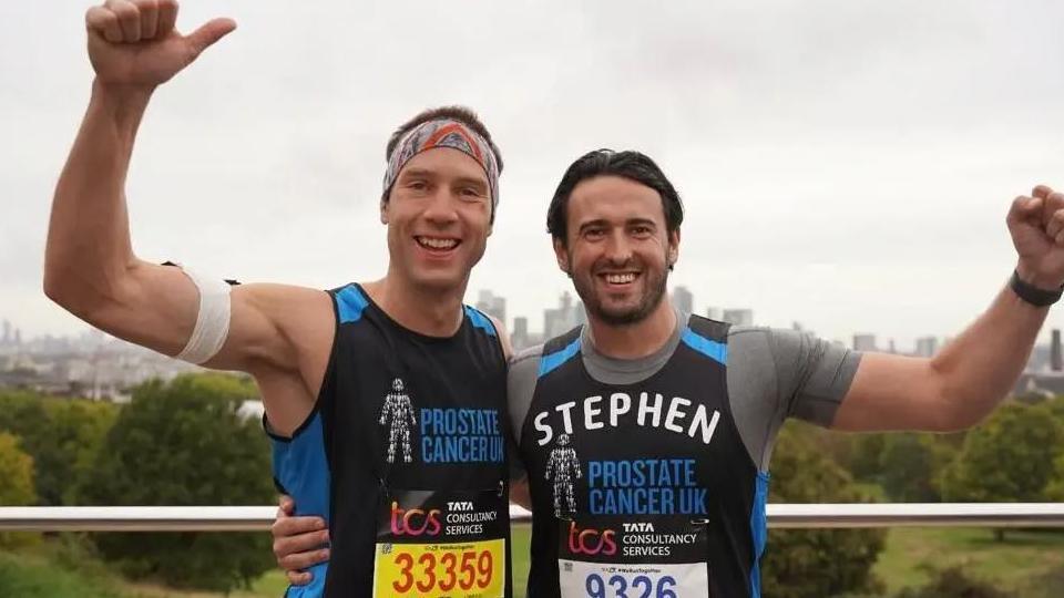 Two men wearing running gear with their arms around each other and each has a fist in the air. 