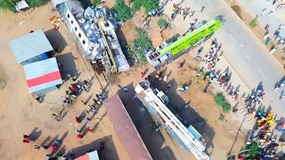 An aerial shot of an overturned train. Two recovery vehicles are parked nearby.