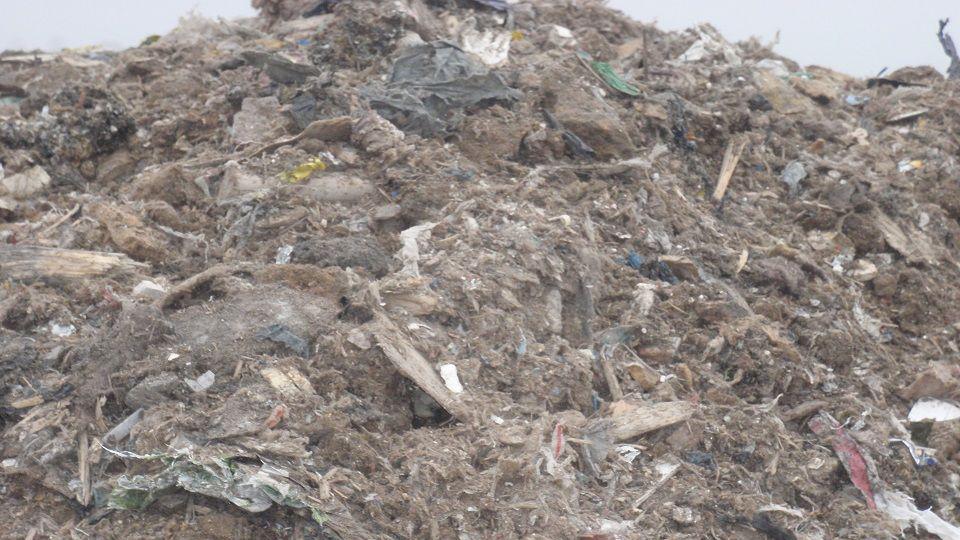 A large pile of waste rotting in a quarry. The waste is hard to work out. It mostly includes bits of plastic, paper, and fibres. 