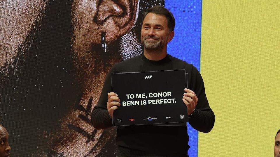 Eddie Hearn holds a card that says 'to me, conor benn is perfect'