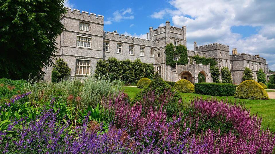 A manor house behind gardens of flowers and hedges 