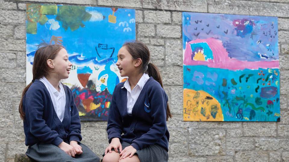 two girls sitting in front of two square boards with paintings on them.